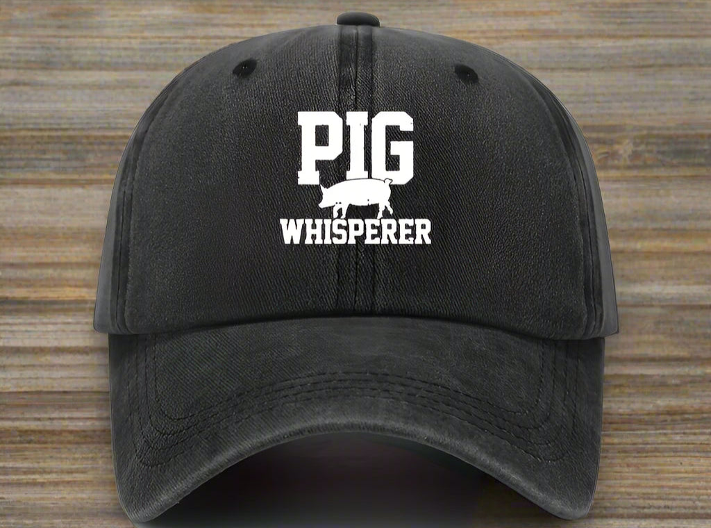 Black cap with 'Pig Whisperer' text and graphic on a white background