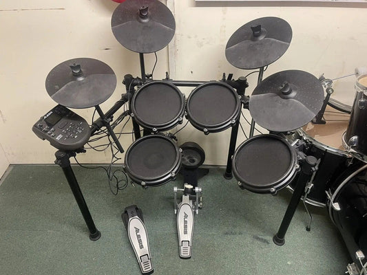 Electronic drum set on a green floor with a white wall background