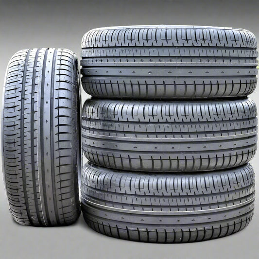Four car tires stacked on a gravel surface with grass in the background