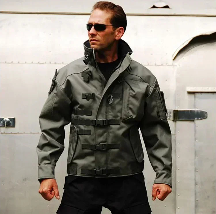 Man wearing a tactical jacket and sunglasses in front of a metallic background