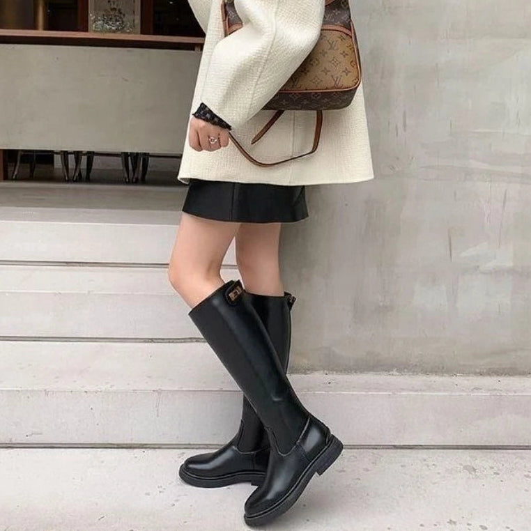 Person wearing black knee-high boots, a white coat, and a brown handbag on a light gray background.