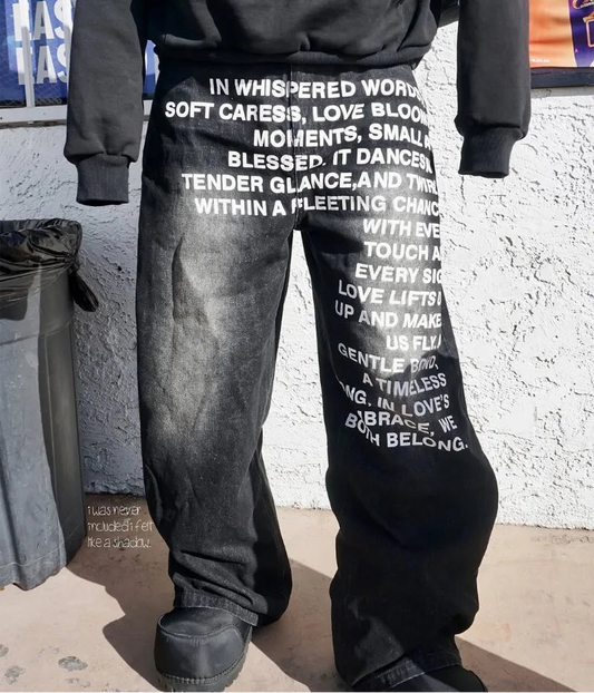 Person wearing black pants with white text against a textured wall.