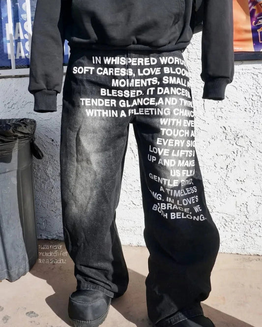 Person wearing black sweatpants with white text against a textured wall.