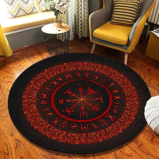 Round rug with red and black design on a wooden floor, with a chair and table in the background.