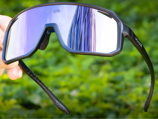 Sunglasses with reflective lenses held against a blurred green background, featuring the Seven brand.