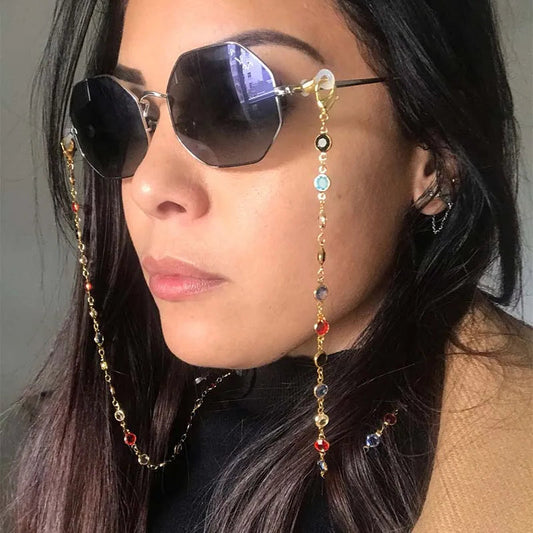 Woman wearing sunglasses with a beaded chain, against a neutral background